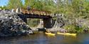 2 cyclists look down on 2 kayaks paddling on the river